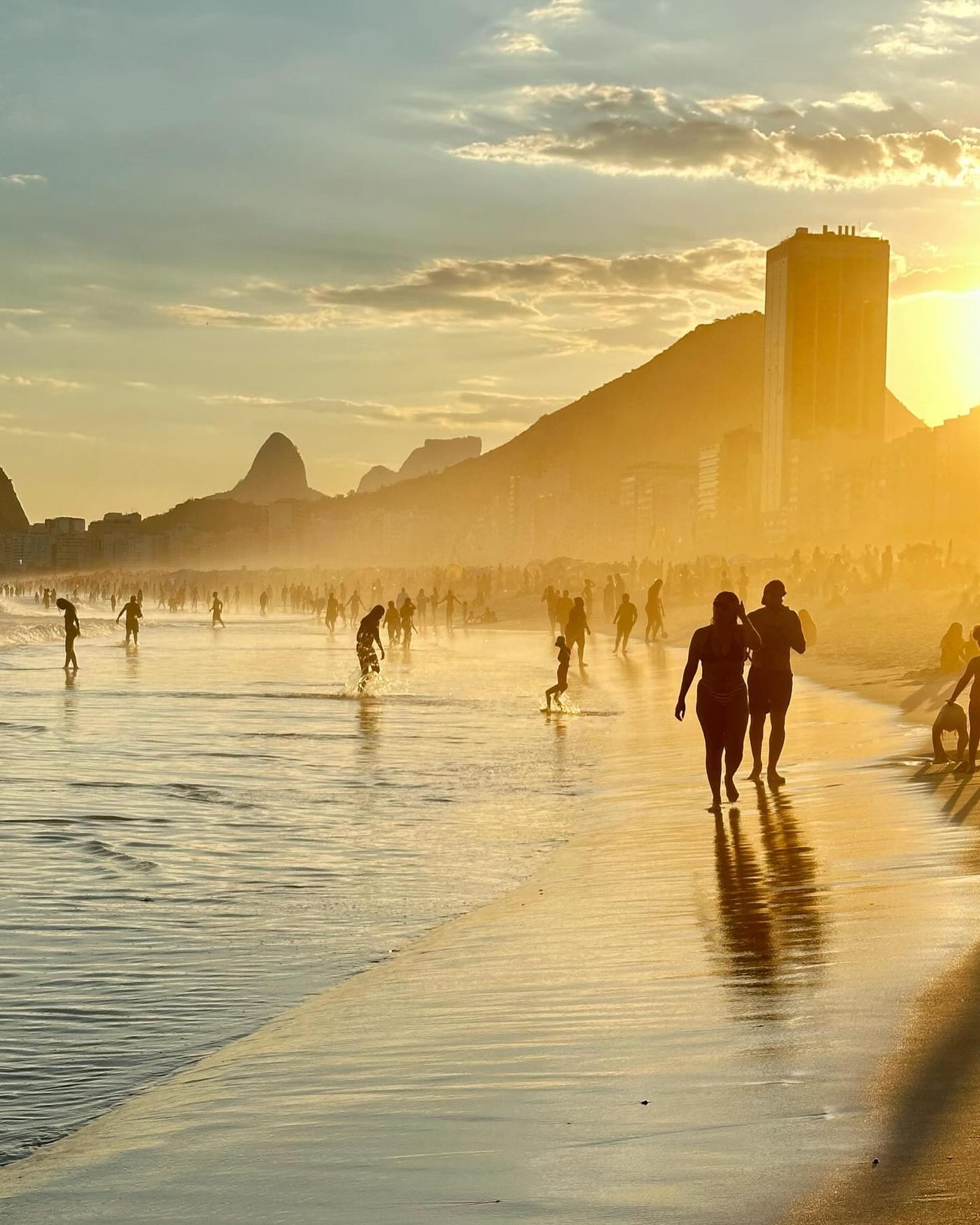 Pessoas caminhando na areia da Praia do Leme ao pôr do sol